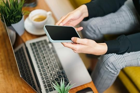 Person using smart phone and laptop at the same time. Coffee and plant on table.