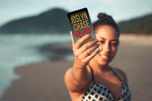 Woman on beach holds up her phone with Joslyn Chase's book, Cincher's Waltz on the screen.
