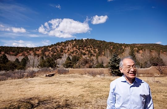 Color photograph of Arthur Sze in a desert field with a low hill dotted with trees in the distance. The sky is a brilliant blue with a few very white clouds.