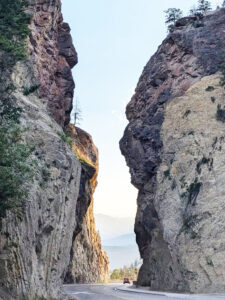 Steep vertical rock walls on each side of a highway with a tiny red vehicle passing between them