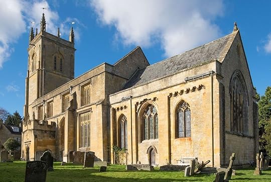 A historic stone church with a tall bell tower, intricate windows, and a surrounding graveyard under a clear blue sky.