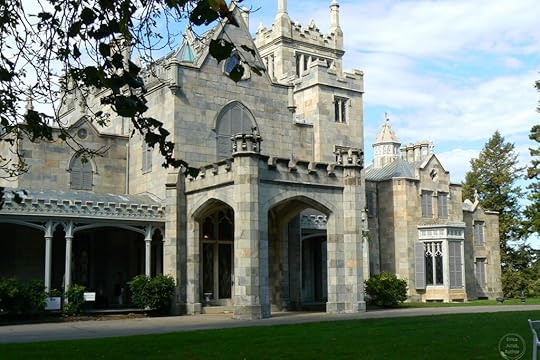 A historic stone castle with intricate architecture, featuring pointed towers, large windows, and a manicured lawn.