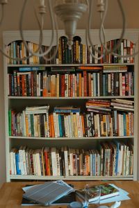 A pale green, overstuffed bookcase in a dining room, with a chandelier in the foreground