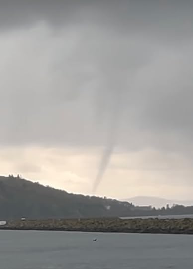 Grey water and grey forested hills over which a grey sky and what seems to be the funnel of a small tornado touching the water