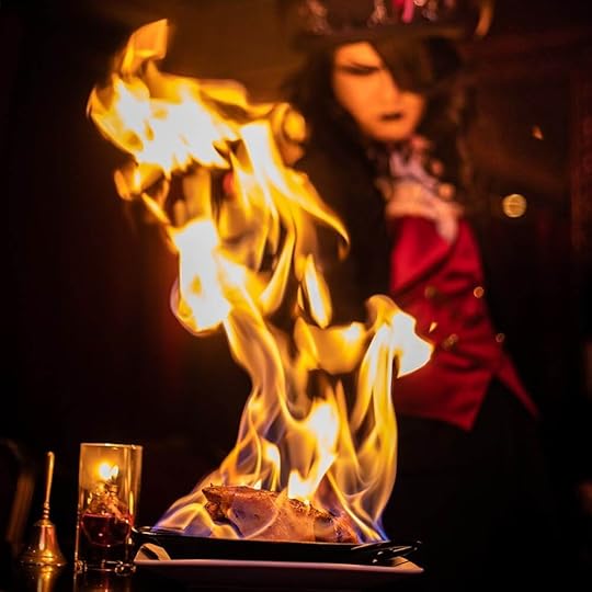 Tokyo's Vampire Cafe, blog post by Aspasia S. Bissas, aspasiasbissas.com. Image is of a Gothic looking server setting a dish on fire, table side.