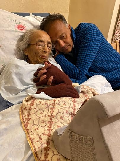 A tender bedside moment with Arvind’s mother, holding hands with a loved one resting his head beside hers.