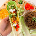 Hand holding a low-carb romaine lettuce taco cup loaded with seasoned beef and toppings