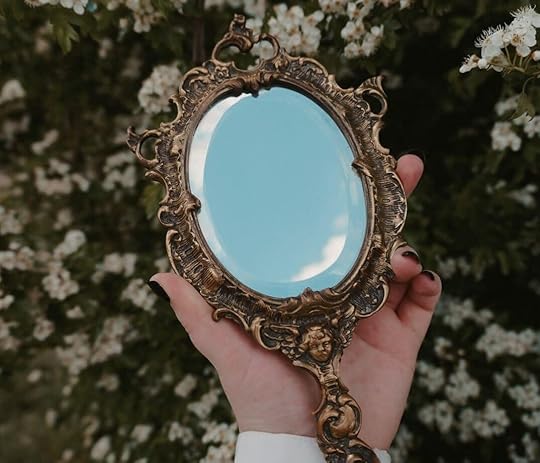 Hand holding ornate antique mirror with flowering bush background