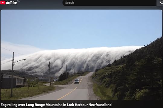 Fog rolling over Long Range Mountains on a sunny day in Lark Harbour, Newfoundland, with a winding road visible in the foreground.