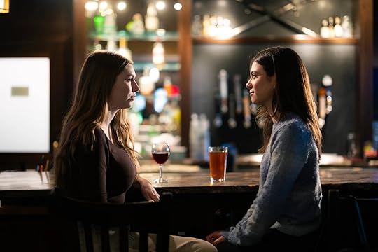 Two women are sitting at a bar, engaged in conversation with drinks in front of them.