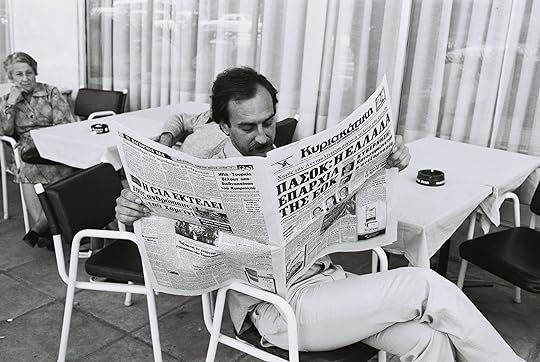 A man reading a newspaper at a café terrace soemwhere (Wikimedia Commons)