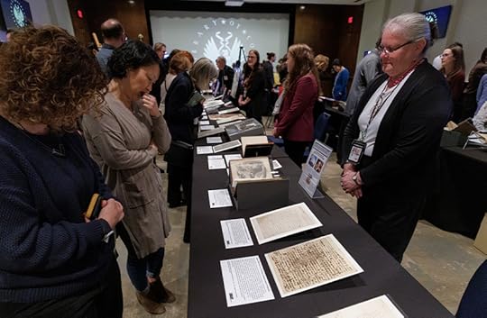 Medium shot of several women standing on opposite sides of a display table laden with several documents.