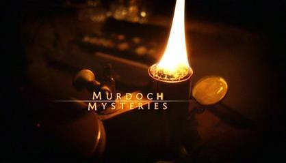 A lit oil lamp with the text 'Murdoch Mysteries' displayed prominently in a dark setting.