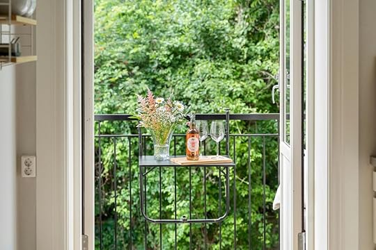 small balcony seen from adjacent room with dropdown table, wine bottle, glass and flowers