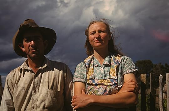 A man and woman, both wearing country working clothes, gaze at the camera, dark clouds in the distance