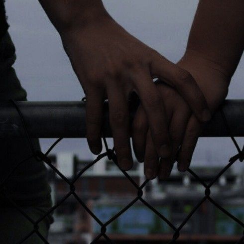 This may contain: two people holding hands over a fence with the city in the background
