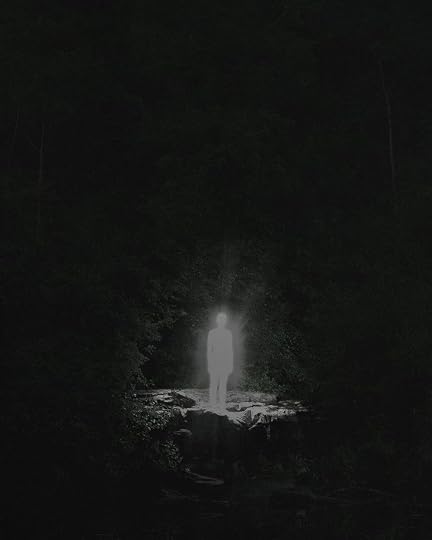 This may contain: a person standing in the middle of a dark forest at night with light coming from their head
