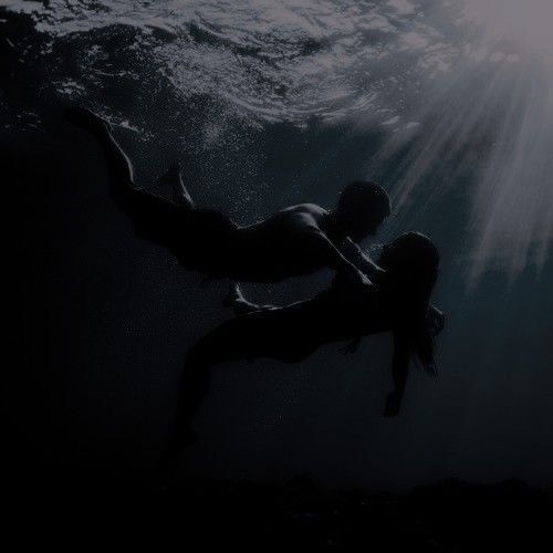 This may contain: a man and woman are swimming under the water in dark waters with sunlight streaming through them