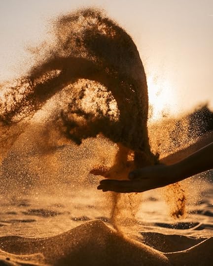 This may contain: someone is throwing sand into the air in the ocean at sunset or sunrise, with their hand reaching for it