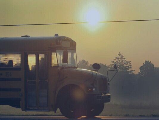 This may contain: a school bus driving down the road at sunset