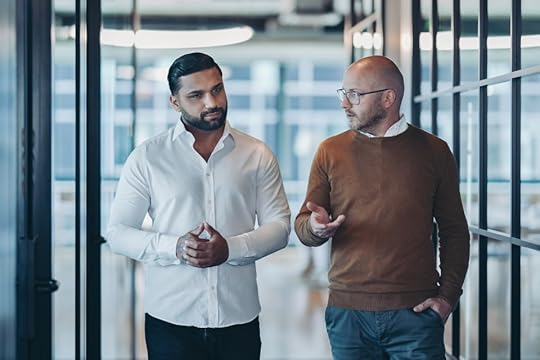 Two men engaged in a conversation while walking through a modern office corridor.