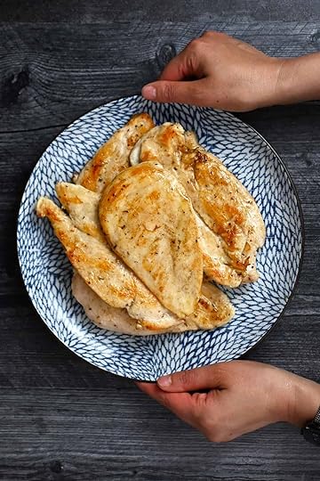 Two hands are holding a blue plate filled with golden brown, perfectly cooked boneless, skinless chicken breasts.