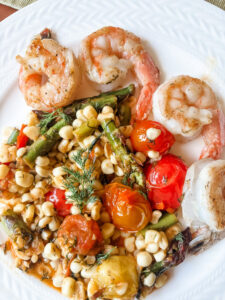 Springtime succotash with lemon and dill served alongside grilled shrimp on a white dinner plate