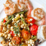 Springtime succotash with lemon and dill served alongside grilled shrimp on a white dinner plate