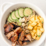 Mango chicken coconut rice bowl topped with fresh mango, sliced cucumber, scallions, and cilantro over coconut lime jasmine rice