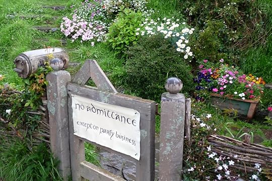 A wooden gate with a sign reading 'no admittance except on party business' surrounded by colorful flowers and greenery.