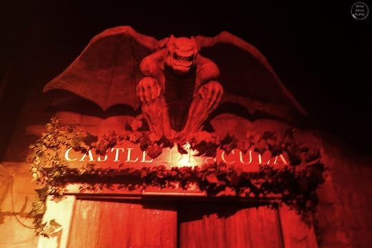 A menacing bat statue perched above the entrance of 'Castle Dracula', illuminated with a red glow and surrounded by ivy.