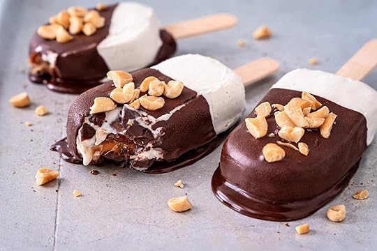Close-up of three Snickers ice cream bars on sticks, topped with chopped peanuts. One has a bite taken, melting slightly