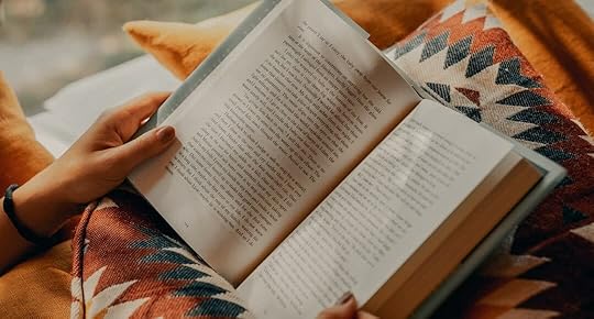 person reading book on brown and beige textile