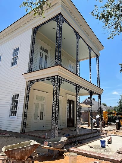 Two-story raised home under construction in West Monroe, Louisiana, with stacked galleries wrapped in black St. Charles-style ornamental ironwork against white siding.