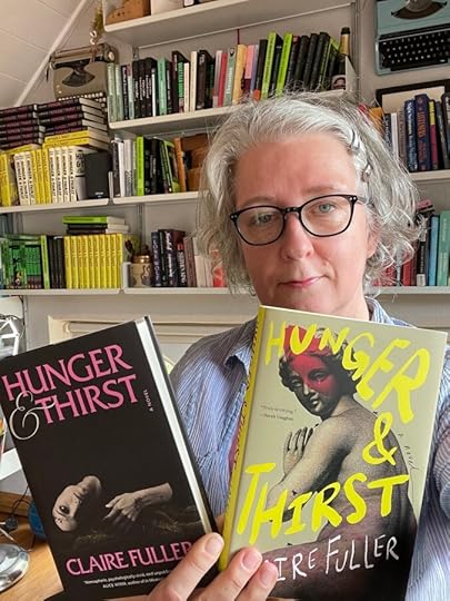 A person holding two copies of the book 'Hunger & Thirst' by Claire Fuller, one with a black cover and the other with a yellow cover. The background features a bookshelf filled with various books.