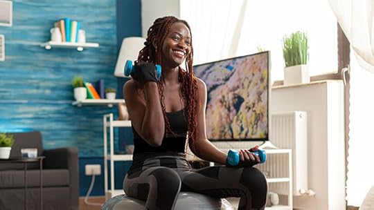 young woman exercises with hand weights while siting atop an exercise ball