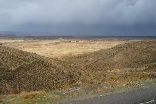 A wide view of a dry landscape with rolling hills and a distant valley, under a cloudy sky indicating possible rain.