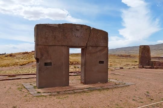 Ancient stone structure with a rectangular opening, featuring carvings on the top, set against a cloudy sky and grassy landscape.