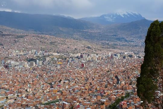 A panoramic view of La Paz, Bolivia, showcasing a densely populated city with a mix of modern and traditional buildings, set against a backdrop of mountains and cloudy skies.