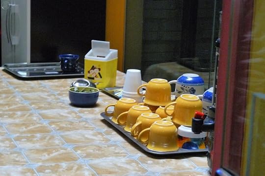 A collection of yellow cups on a tray beside a blue bowl and a container on a kitchen table with a patterned surface.