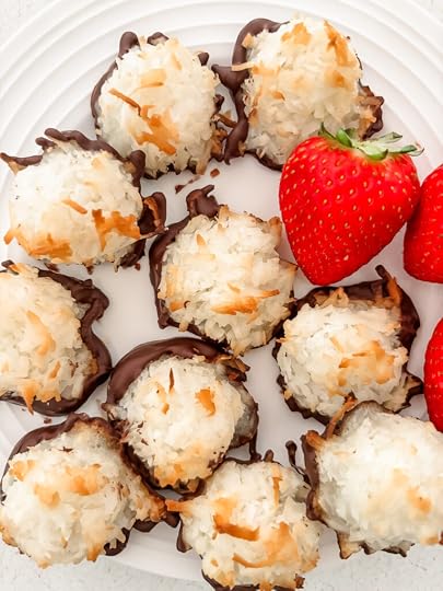 Close-up of a chocolate-dipped coconut macaroon showing its golden toasted exterior and dark chocolate base with strawberries
