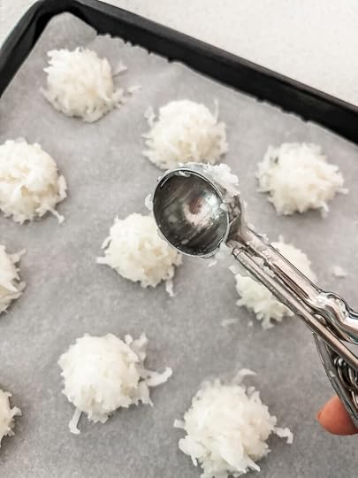 Using a melon baller to shape coconut macaroon mixture into uniform balls on a parchment-lined baking sheet