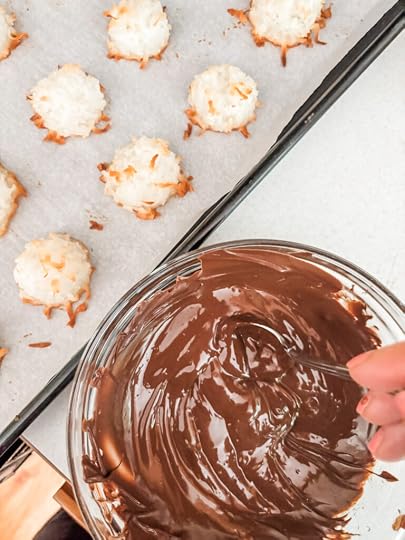  Dipping the bottom of a baked coconut macaroon into a bowl of melted chocolate