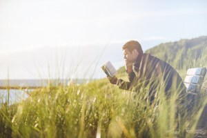 Man engrossed in reading as he sits on a seaside bench.