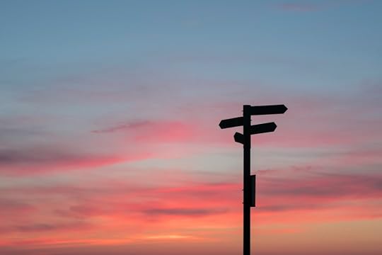 A signpost with four signs pointing in different directions stands silhouetted against a crimson and blue sunset.