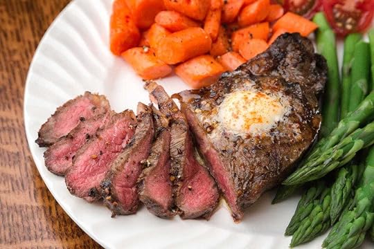 Ribeye steak with butter and asparagus and carrots on the side on a white plate.
