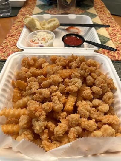 A fried shrimp dinner in a takeaway container. In addition to the shrimp, there is a dinner roll, Cole slaw, French fries and cocktail sauce.
