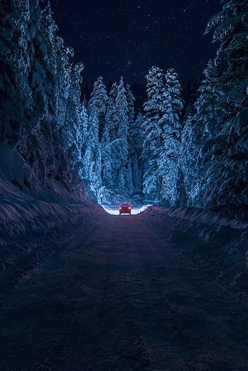 This may contain: a car driving down a snowy road at night with the headlights on and trees covered in snow