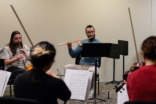 Several musicians sit while playing, arranged in a circle in a room.