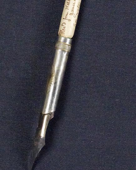 Close up photograph of a 19th-century pen. The tip is metal; the middle appears to be made of bone or ivory with writing carved into it. 